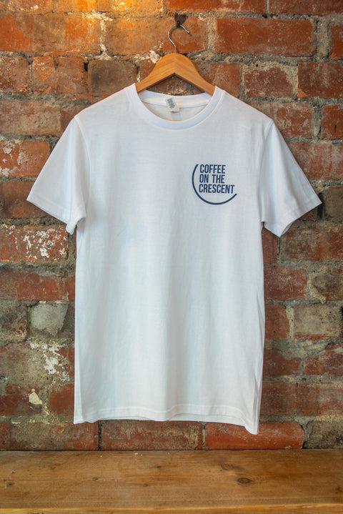 A Coffee On The Cresent T Shirt ion. a hanger against a brick wall. The COTC branding clearly visible on the left breast.